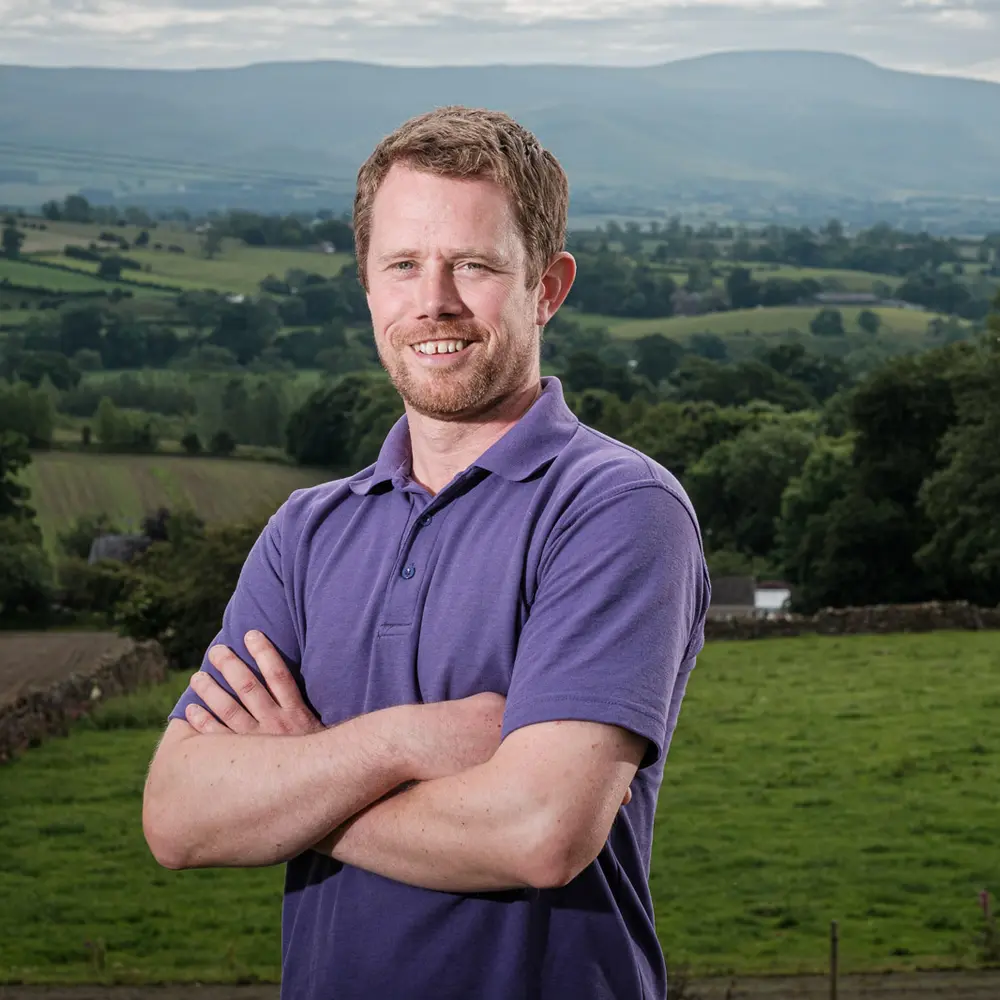 Cumbrian dairy farmer James Tweedie standing in a field with hills in the distance.