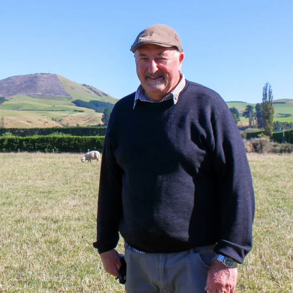 New Zealand sheep farmer Warwick Green standing in a field with blue sky in the background.