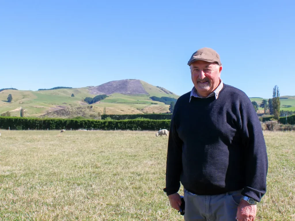 New Zealand sheep farmer Warwick Green standing in a field with blue sky in the background.