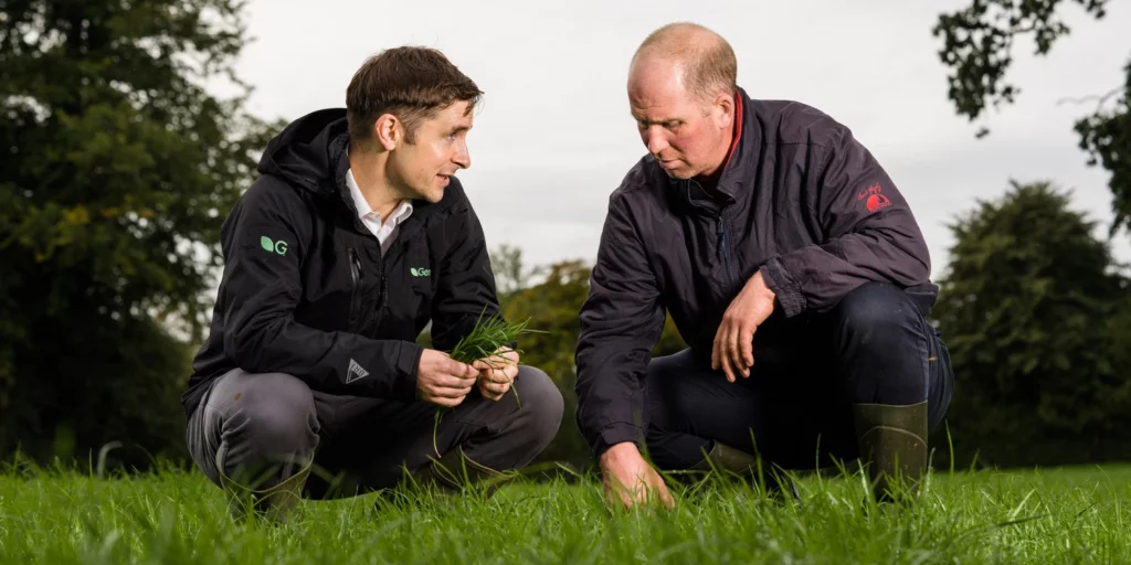 Germinal grass expert Diarmuid Mutphy crouches in pasture with a livestock farmer